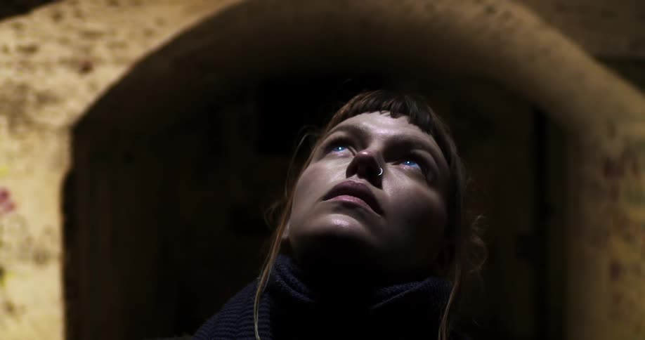 Woman raises her head and looks up at the light in an abandoned tunnel