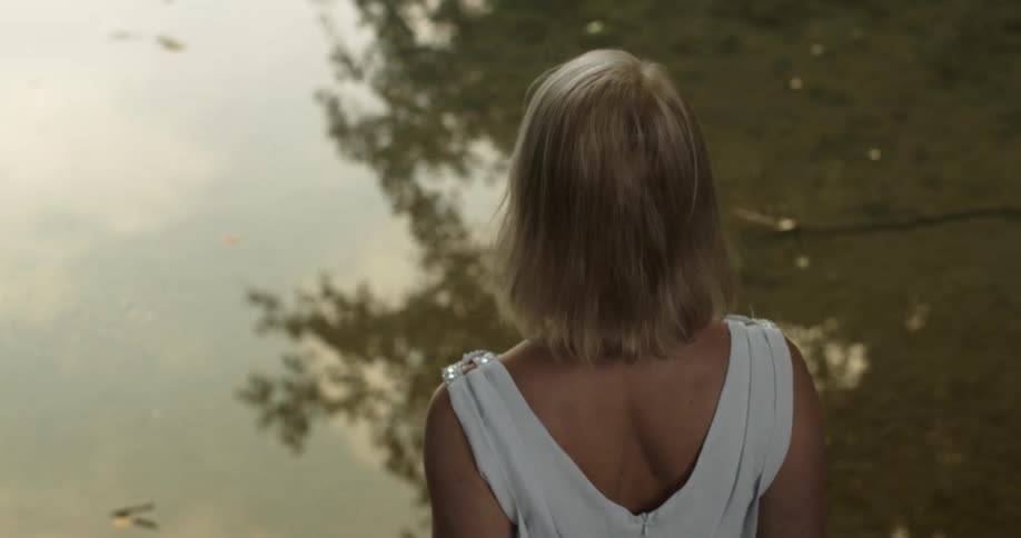 A woman wearing a dress stands by the shore of a body of water