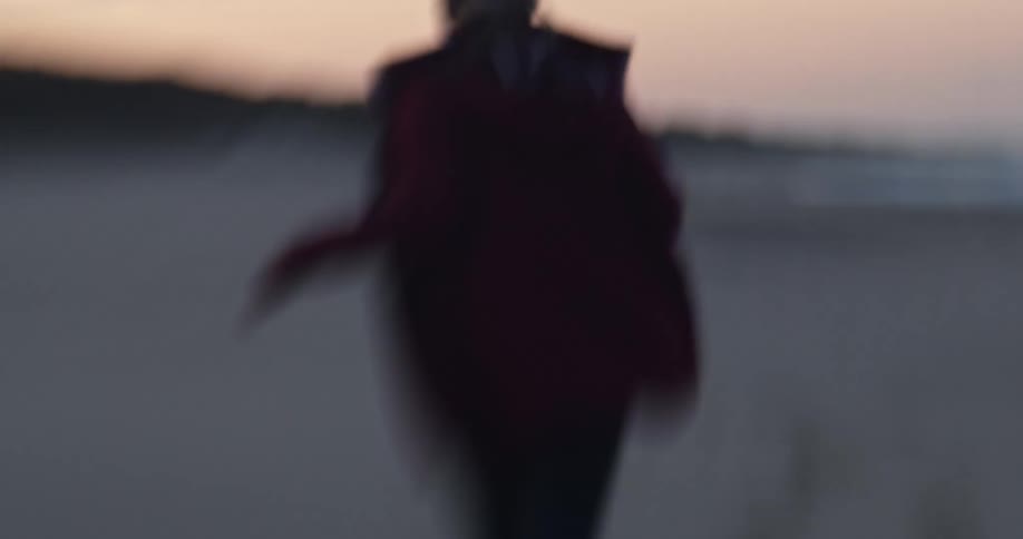 Woman wearing red coat runs across beach towardocean