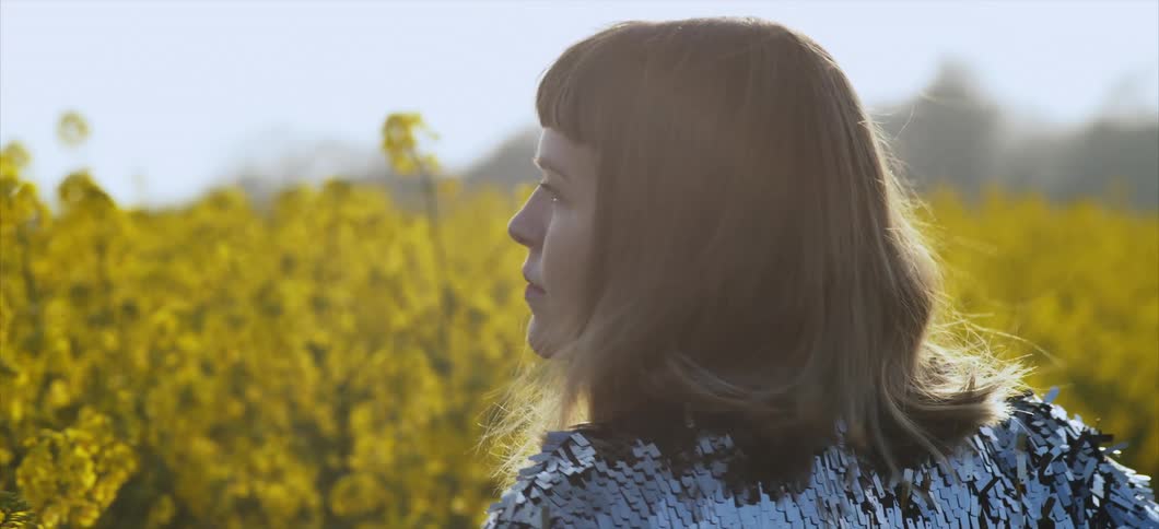 A woman walks through a field of yellow flowers