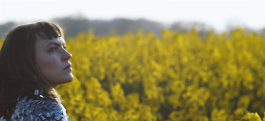 A woman walks through a field full of yellow flowers