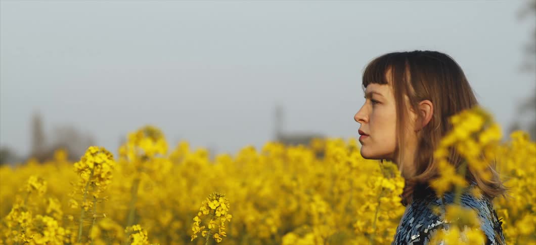 The woman looks around in a field of yellow flowers