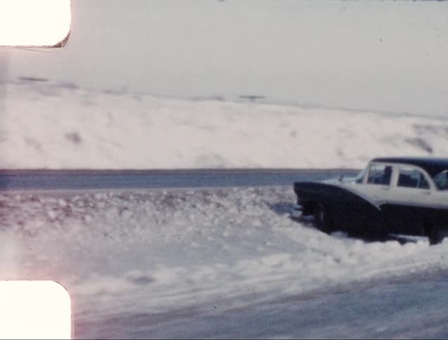 Cars travel past a car stuck in the snow of a median strip