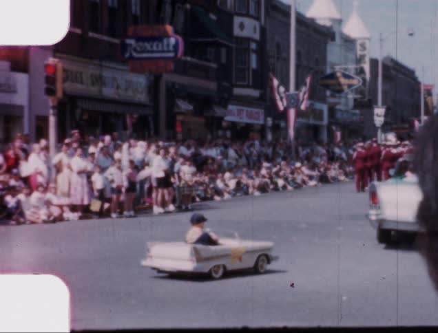 A young boy drives a small car on a street during a parade