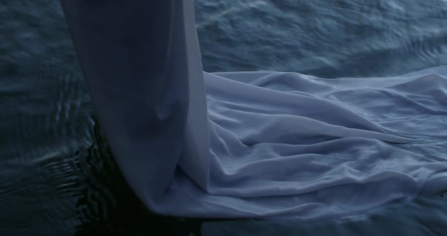 A woman drags the train of her white dress through water