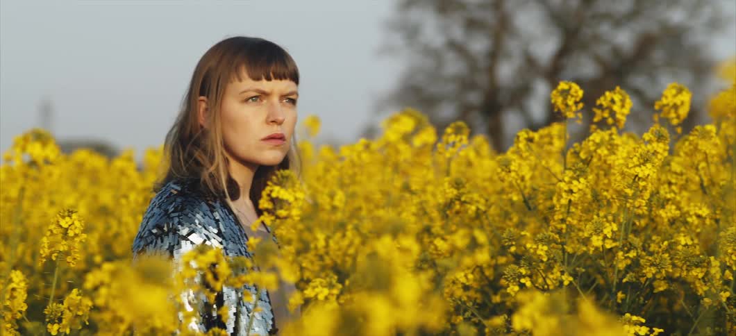 A white woman stands in a field of flowers and looks around at her surroundings