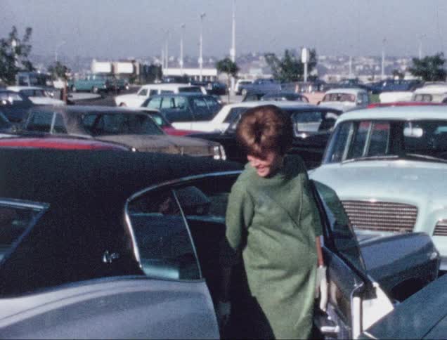 A woman smiles and looks back as she gets into the passenger side of a car