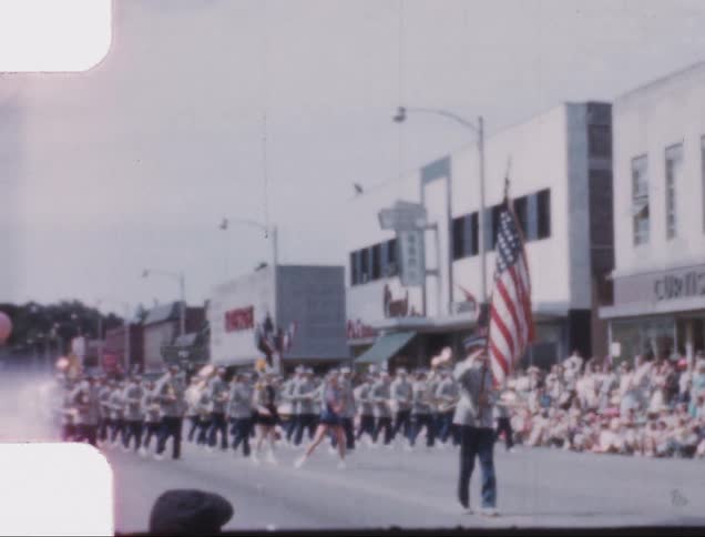 A cop shakes a kid as a band marches down the street during a parade