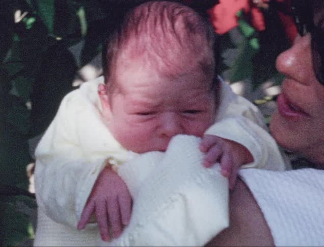A young mother smiles as she holds her infant child outdoors