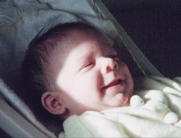 A baby playing moving its arm while lying in a stroller