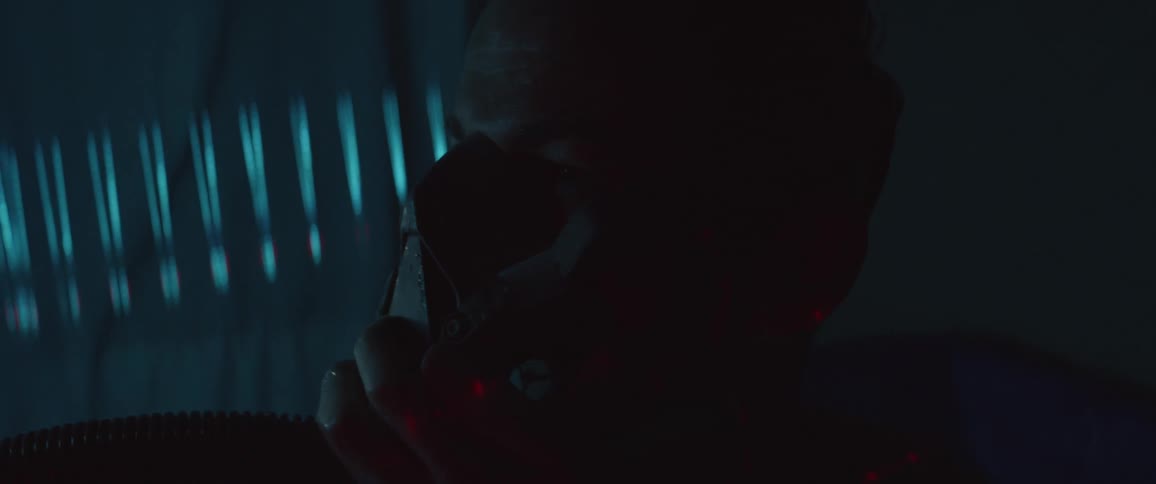 A white man sits in a dark room holding a mask to his face