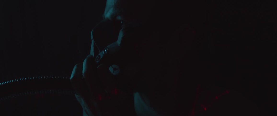 Bare chested man wearing breathing mask in dark room reaches up to grab apparatus