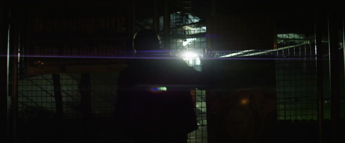 A man stands near a caged area and puts his hand on the metal frame
