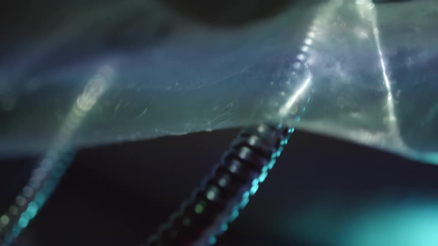 A pair of metal cables running under a sheet of plastic into a flashing connection with a device