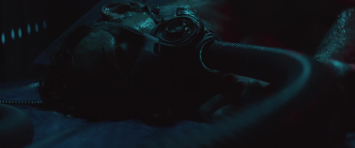 A sweating man in a breathing mask attached to a tube lying on a plastic sheet in a dark room