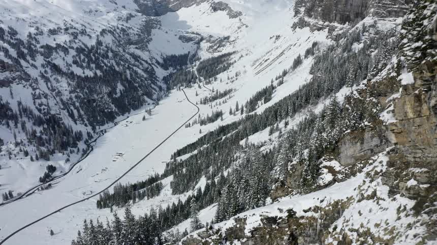 A mountain range and valley with a road covered in snow