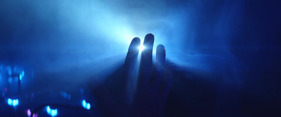 A hand cloaked in shadow rising to block a stream of light in a dark foggy room