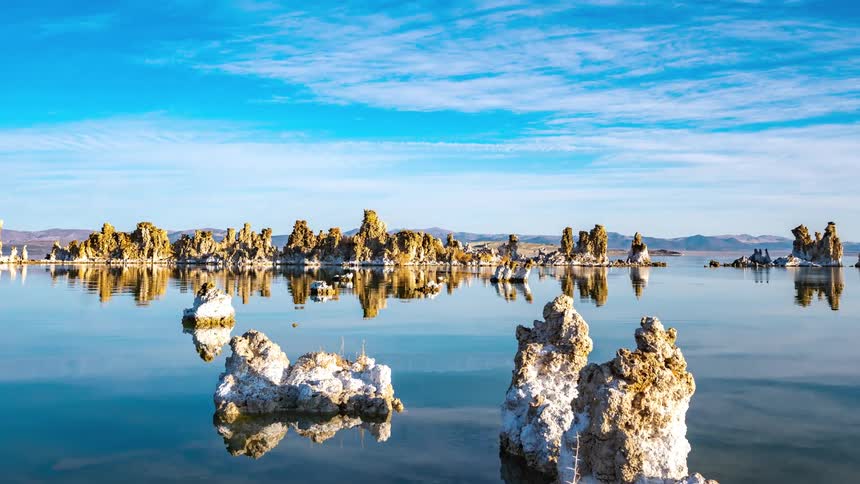 Bright azure sky reflects on mirror like water dotted with rock formations