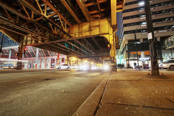 Cars and pedestrians travel beneath a city overpass at night