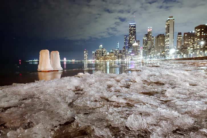 Ice on the rocks and harbor shore with a glowing city skyline