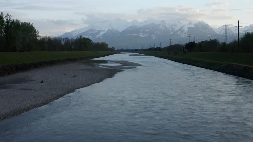 A narrow river surrounded by forest leads to a mountain range