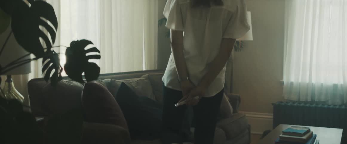 A woman sits on top of her husband who is laying on a couch and shows him a pregnancy test