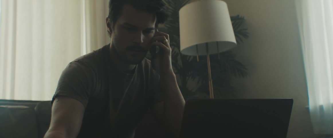 A man talks on a smartphone while writing in a notepad on a living room table