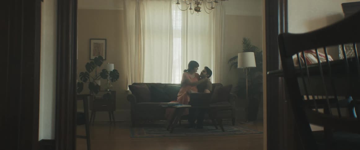 Pregnant woman walks into room joining man on couch