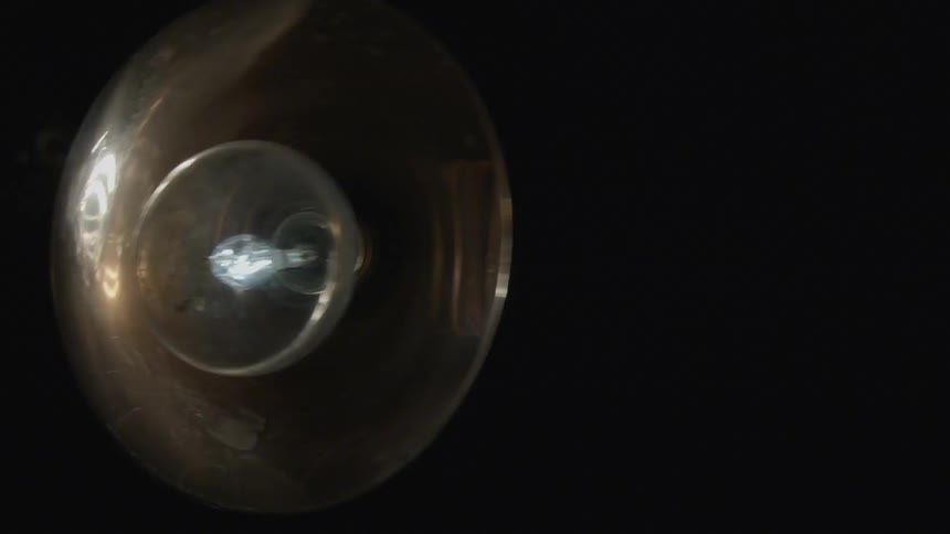 A light bulb in a metal shade swings back and forth