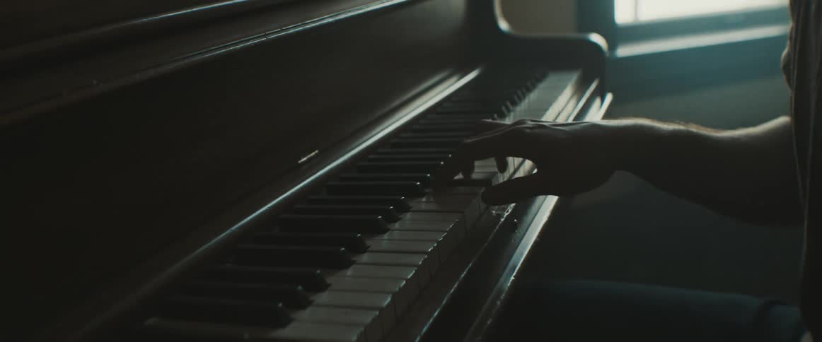 A man sits in a dark room playing the piano