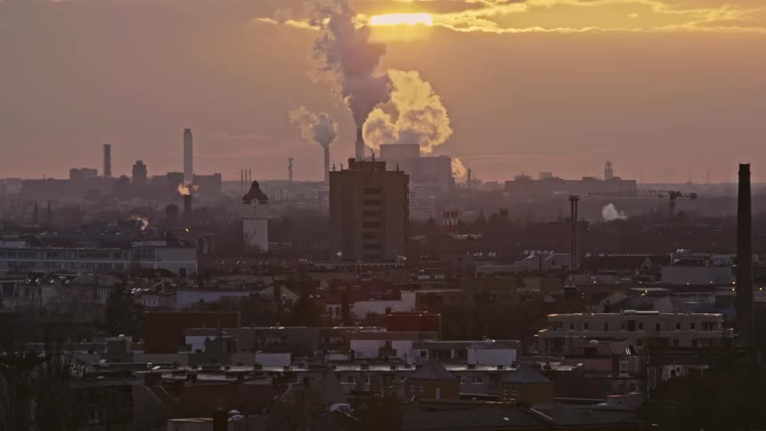 Smoke billows out of a factory in a city skyline