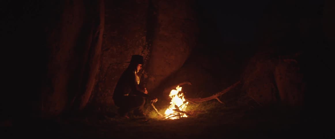 A white woman stokes a campfire outdoors