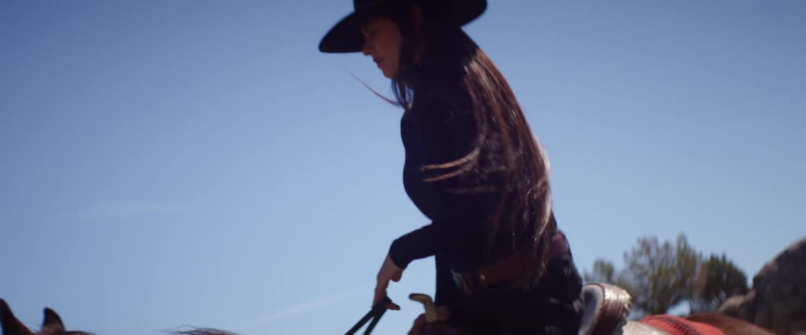 A woman in a black cowboy hat climbing into the saddle of a horse