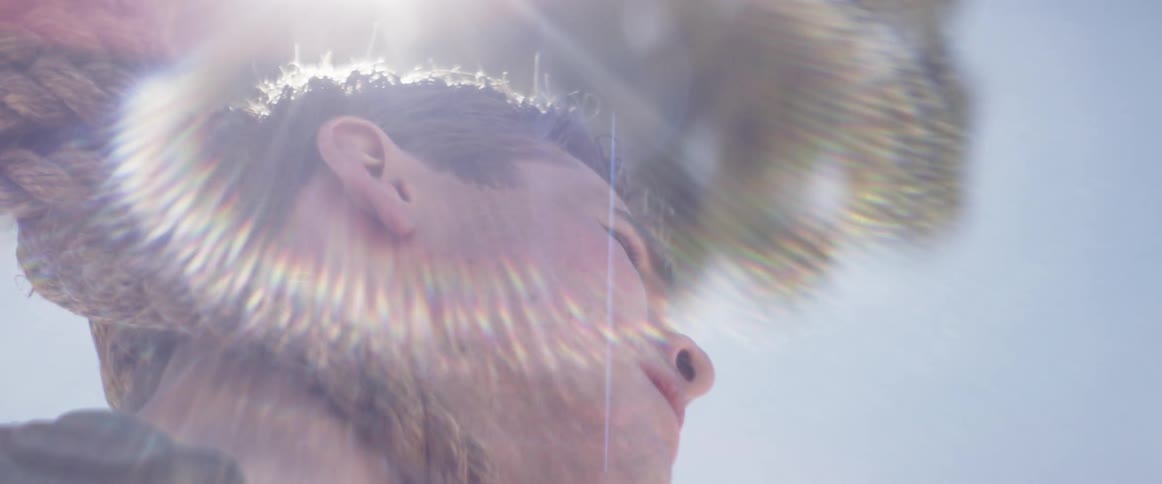 A man gaining consciousness and looking around as he discovers a noose is tied around his neck