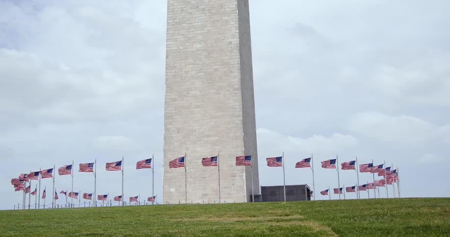 A tall monument surrounded by waving american flags in a field under a blue sky