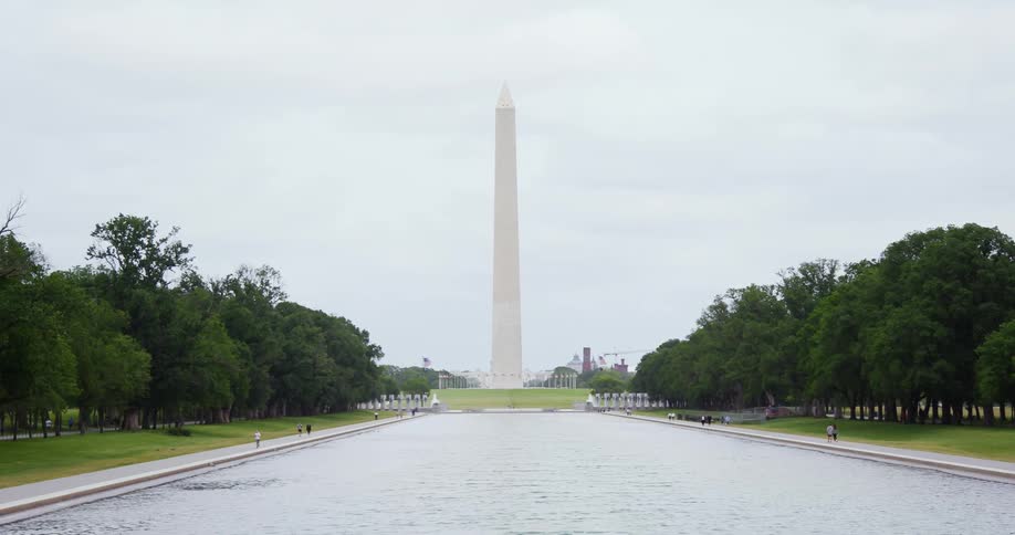 People walking along the water in front of a monument