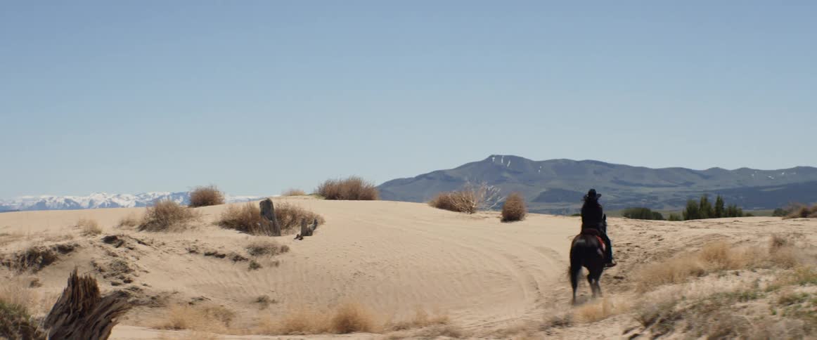 A woman rides her horse up a sandy hill
