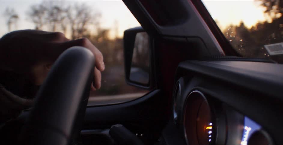 Black man drives a car in the countryside at sunset