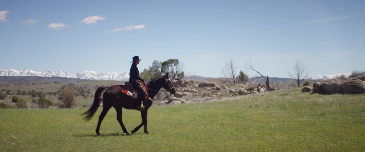 A woman rides her horse on a ranch with views of a mountain range