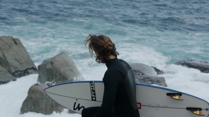 A surfer walks along a beach holding a surfboard