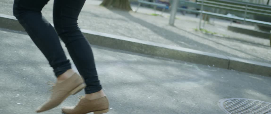 A white woman runs through a city park in jeans and hard shoes