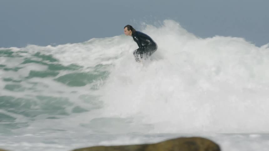 Surfer rides crashing wave near rocks