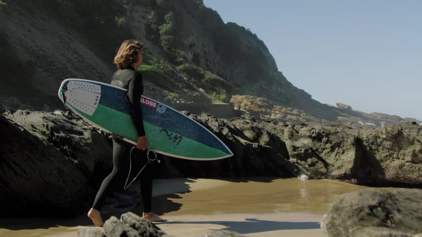 A male teenager walks to the water with his surfboard