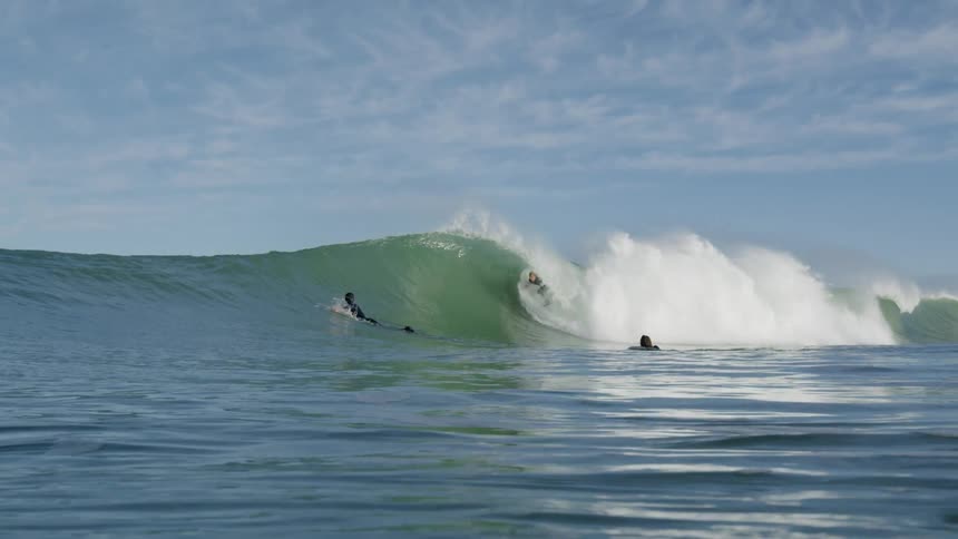 A group of surfers surf a wave as it comes towards land