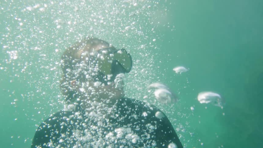 A diver with goggles floats to the top of a body of water