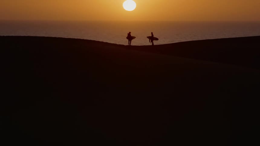 Two surfers stand on a beach facing each other