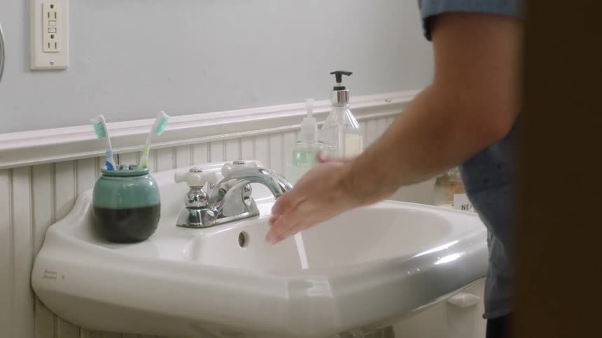 A white male washes his hands in a bathroom sink