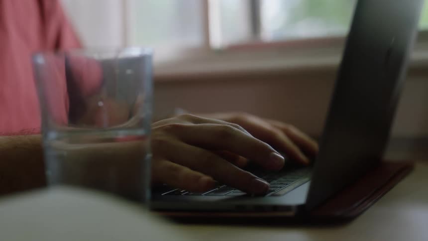 Man at home works on a laptop near a window