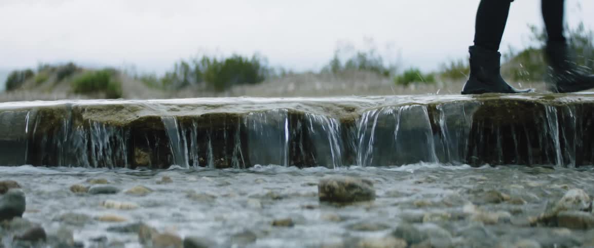 A person in boots walks over a small waterfall