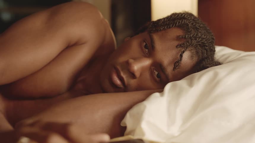 A black man looks at his smartphone while in bed